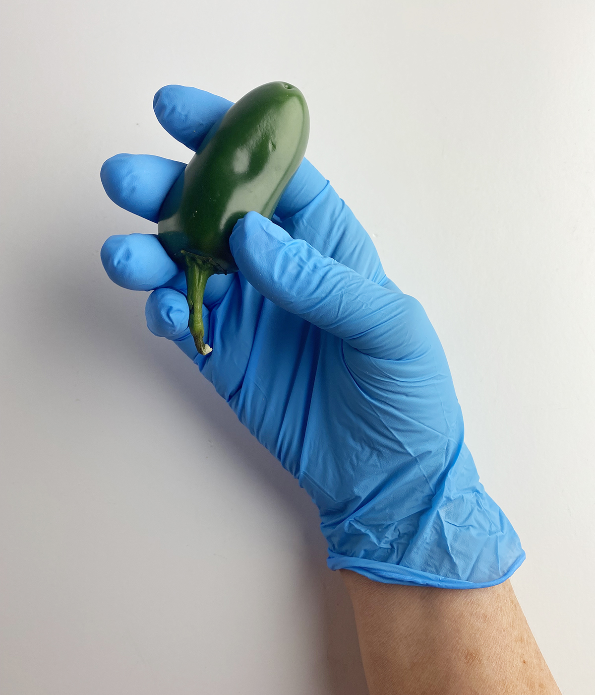 Hand in a surgical glove holding a pepper.