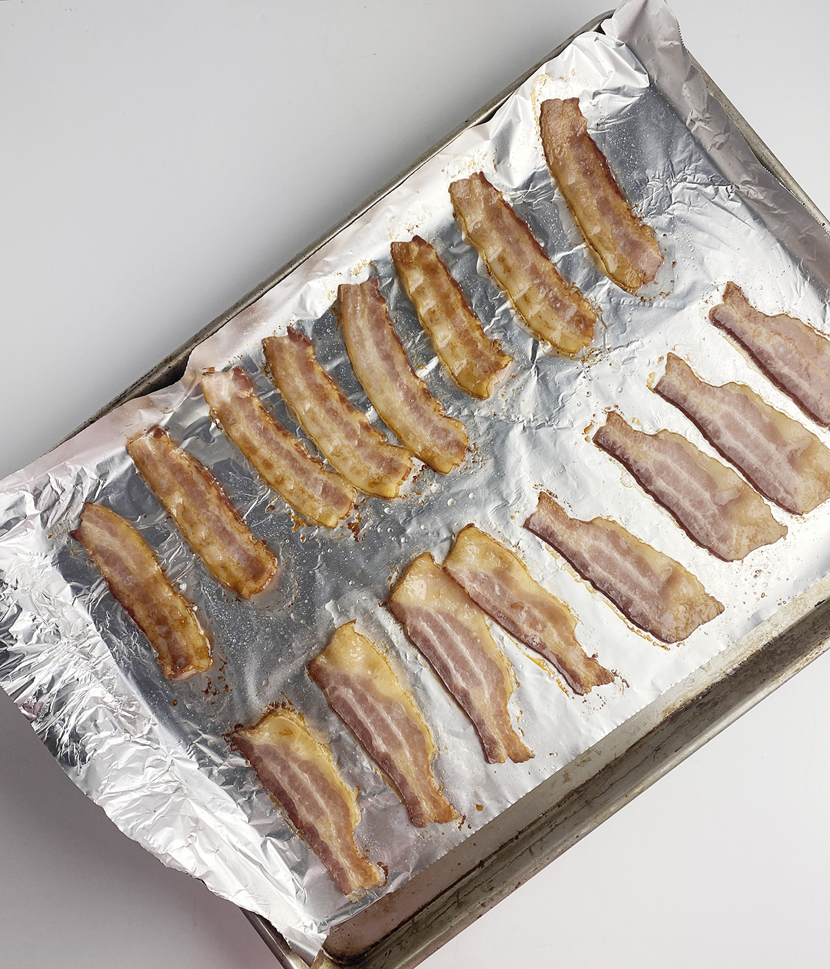 Partially cooked bacon on a foi llined baking sheet.