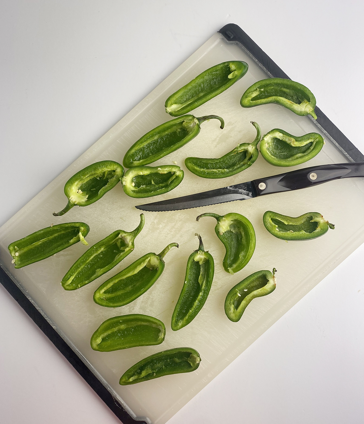 Sliced and seeded jalapenos on a cutting board with a knife.