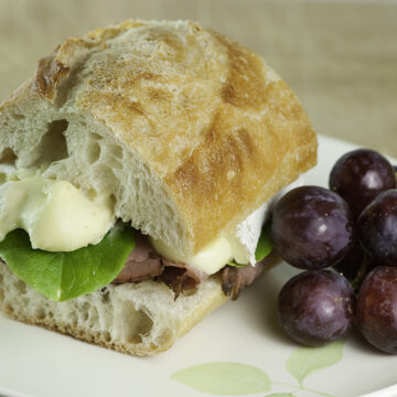 Roast Beef and Brie Sandwich with grapes on a plate.