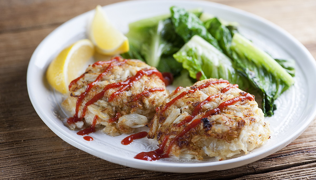 Baked crab cakes on a plate with hot sauce.