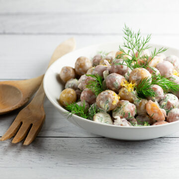 Sour cream potato salad in a bowl with serving utensils.